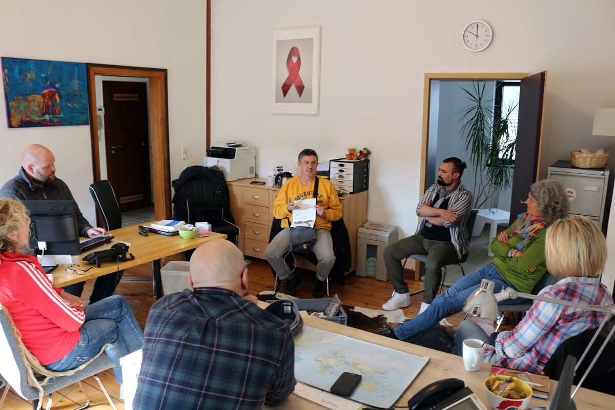 Thorsten Höller zeigt dem Aids-Hilfe-Team einen Lieferschein auf dem Pride Merch Shop und erklärt, wie er diese Bestellung bearbeitet