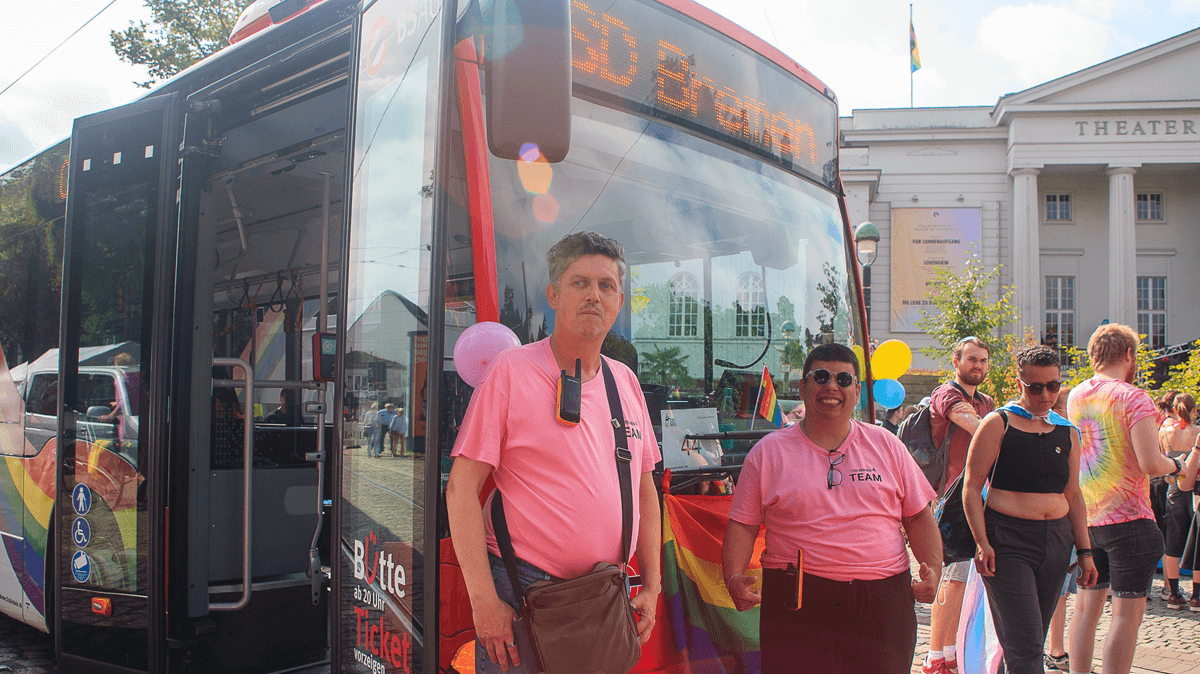 Thorsten und Timmi stehen vor einem BSAG-Bus. Der BSAG-Bus ist mit einer Regenbogenflagge geschmückt und auf der Anzeigetafel steht CSD Bremen